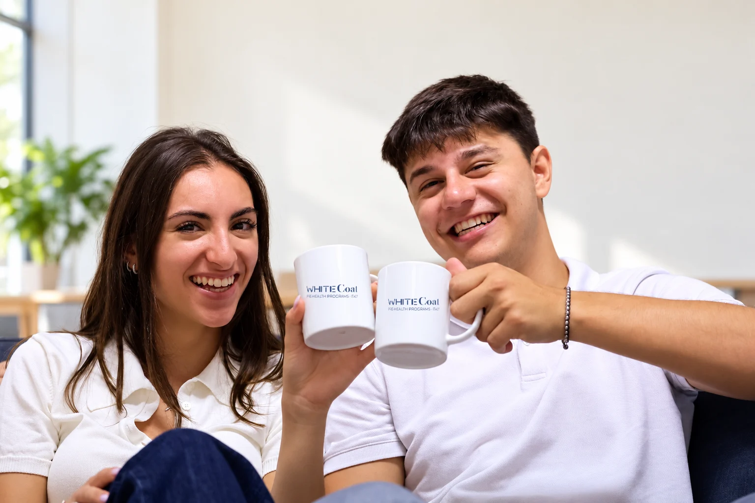 Two pre-health students toasting with White Coat mugs during a break on campus